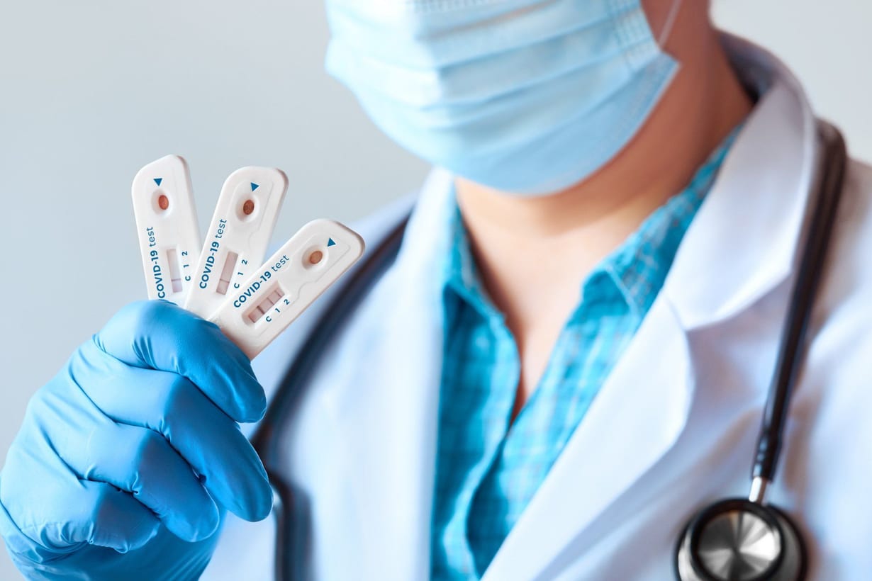Un operatore sanitario con guanti e mascherina mostra due test rapidi